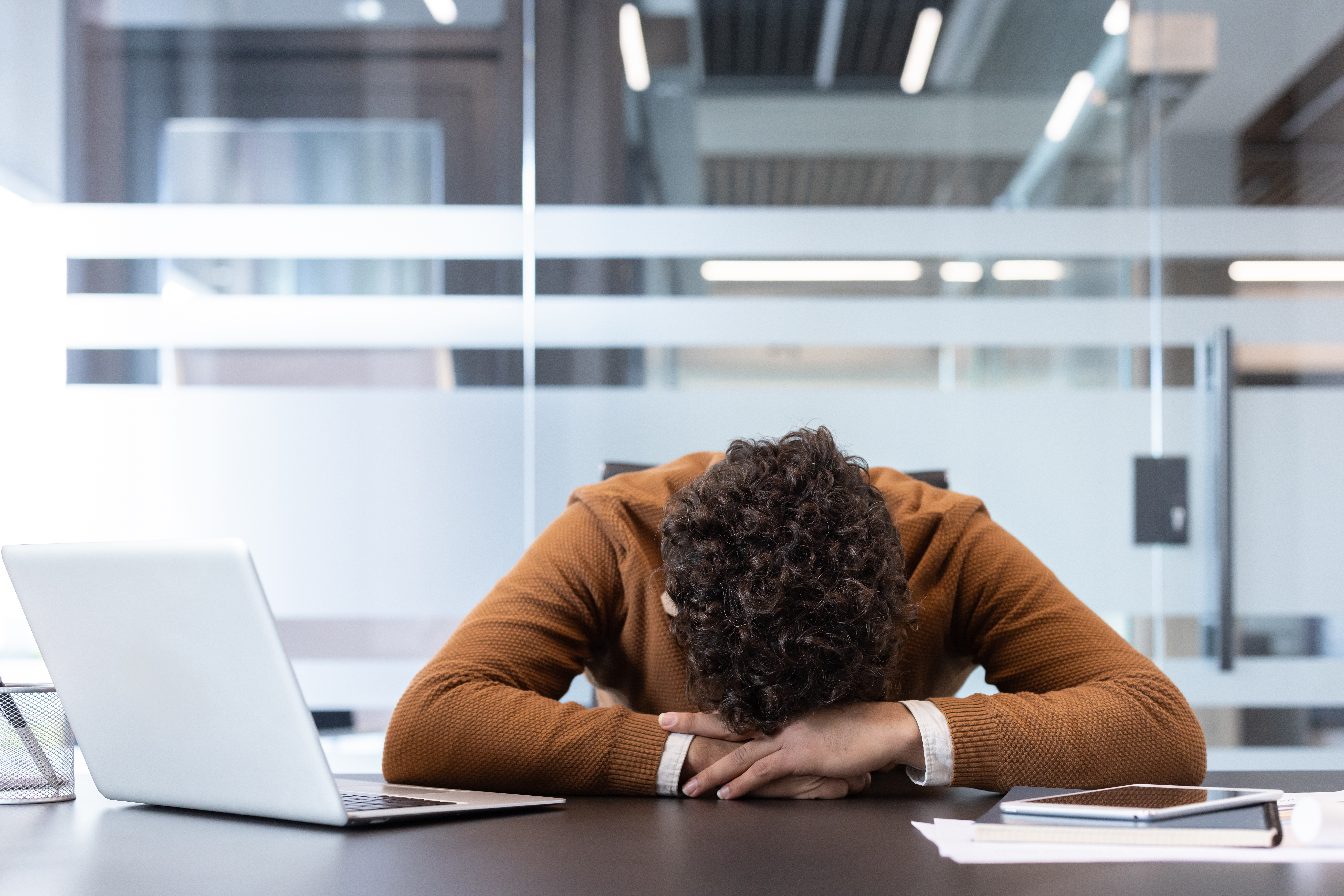 A sad person rests his head on their arms atop a desk, thinking about his career success.